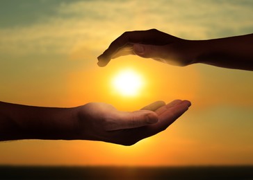 Image of Man and woman holding hands against sun in sky at sunset, closeup