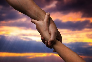 Image of Man and woman holding hands against sky at sunset, closeup