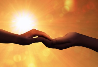 Image of Man and woman holding hands against sky with bright at sunset, closeup