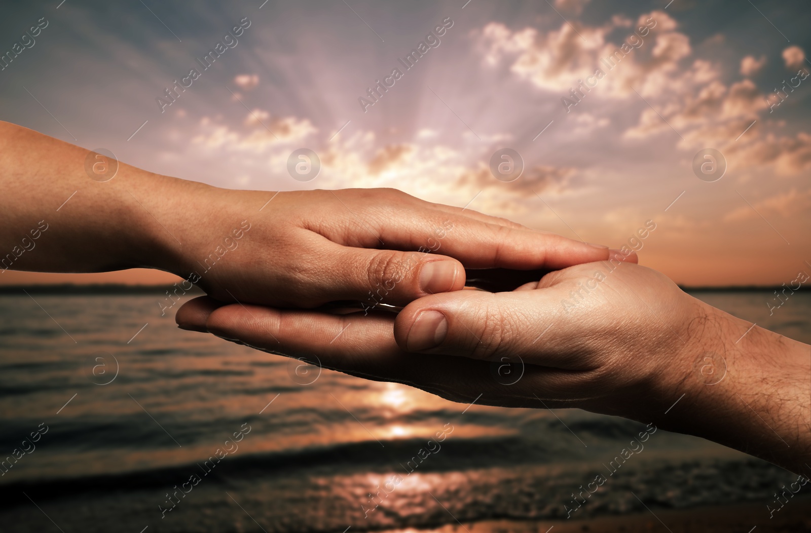 Image of Man and woman holding hands against seascape at sunset, closeup