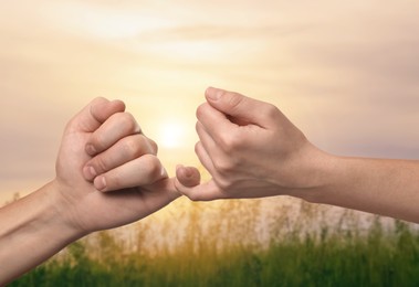 Image of Man and woman holding little fingers against green field at sunset, closeup of hands