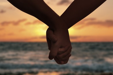 Image of Man and woman holding hands against seascape at sunset, closeup