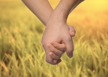 Image of Man and woman holding hands against green grass, closeup