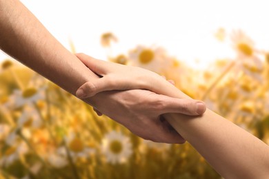 Image of Man and woman holding hands against flowers at sunrise, closeup
