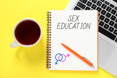 Image of Sex Education inscription, male and female symbols in notebook, pen, laptop and tea on yellow background, top view
