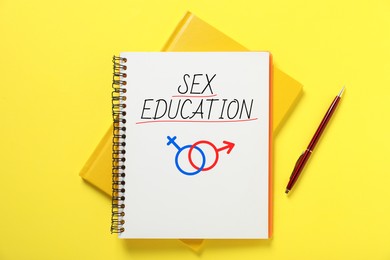 Image of Sex Education inscription, male and female symbols in notebook and pen on yellow background, top view