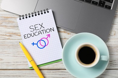 Image of Sex Education inscription, male and female symbols in notebook, pen, coffee and laptop on wooden table, top view