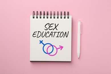 Image of Sex Education inscription, male and female symbols in notebook and pen on pink background, top view