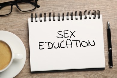 Image of Sex Education inscription in notebook, pen, glasses and coffee on wooden table, top view
