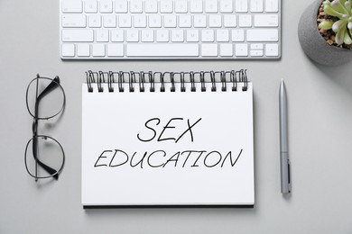 Image of Sex Education inscription in notebook, pen, glasses and computer keyboard on grey table, top view