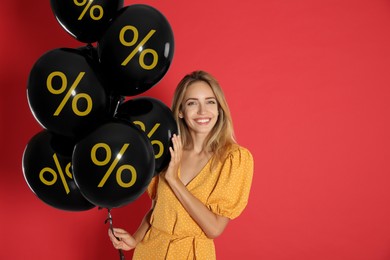 Image of Happy woman holding balloons with percent signs against red background. Hot sale, special offer