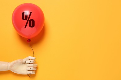 Image of Red balloon with percent sign in mannequin's hand on orange background. Hot sale, special offer