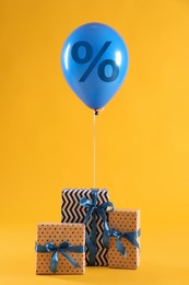 Image of Blue balloon with percent sign and gift boxes on orange background. Hot sale, special offer