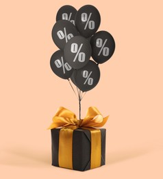 Image of Black balloons with percent signs and gift box on pink beige background. Hot sale, special offer