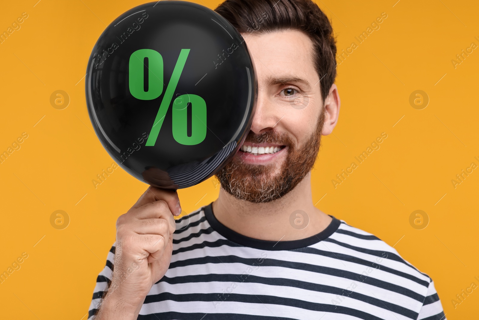 Man holding balloon with percent sign near his face against orange background. Hot sale, special offer Image of Man holding balloon with percent sign near his face against orange background. Hot sale, special offer