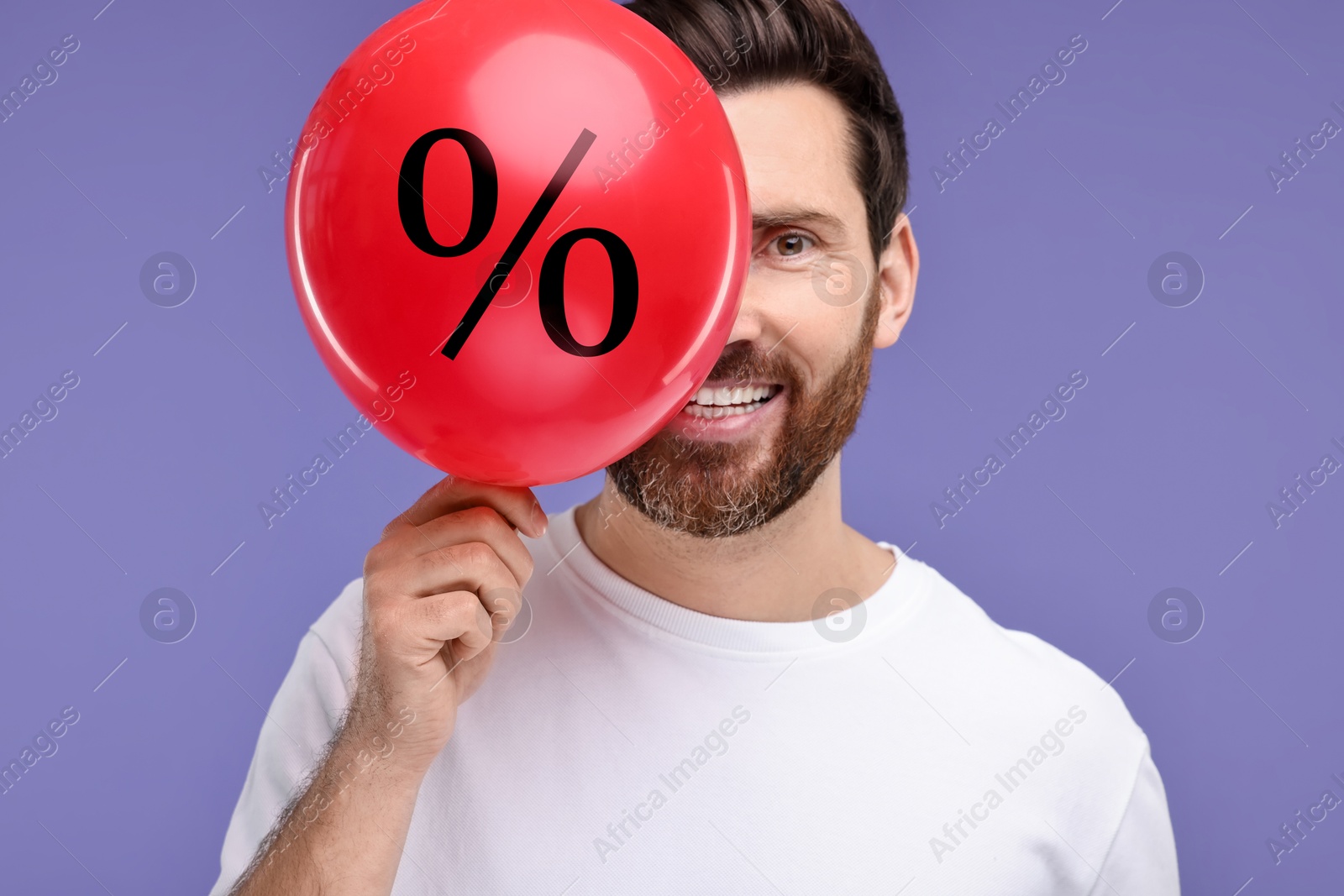 Man holding balloon with percent sign near his face against purple background. Hot sale, special offer Image of Man holding balloon with percent sign near his face against purple background. Hot sale, special offer