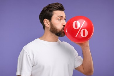 Image of Man inflating red balloon with percent sign against purple background. Hot sale, special offer
