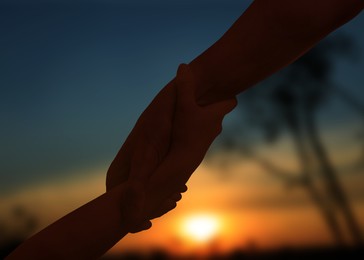Image of Man and woman holding hands in nature at sunset, closeup