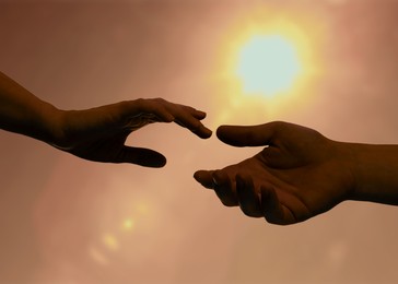 Image of Man and woman reaching to each other against sky with bright sun at sunset, closeup of hands