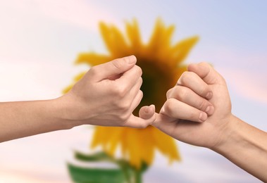 Image of Man and woman holding little fingers against sunflower, closeup of hands