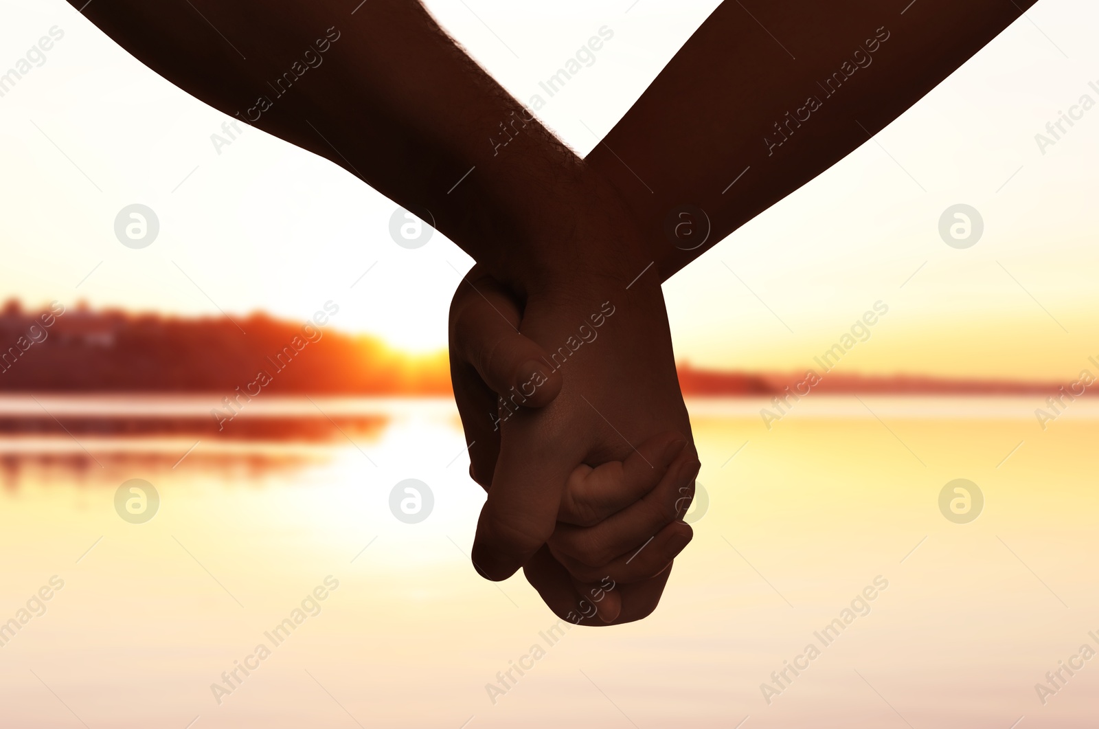 Image of Man and woman holding hands against seascape at sunset, closeup