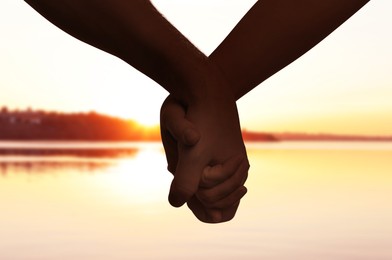 Image of Man and woman holding hands against seascape at sunset, closeup