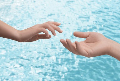 Image of Man and woman reaching to each other against seascape, closeup of hands