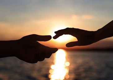 Image of Man and woman reaching to each other against seascape at sunset, closeup of hands