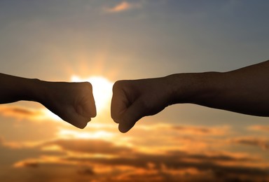 Image of Man and woman making fist bump against sky at sunset, closeup of hands