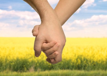 Image of Man and woman holding hands against green field on sunny day, closeup