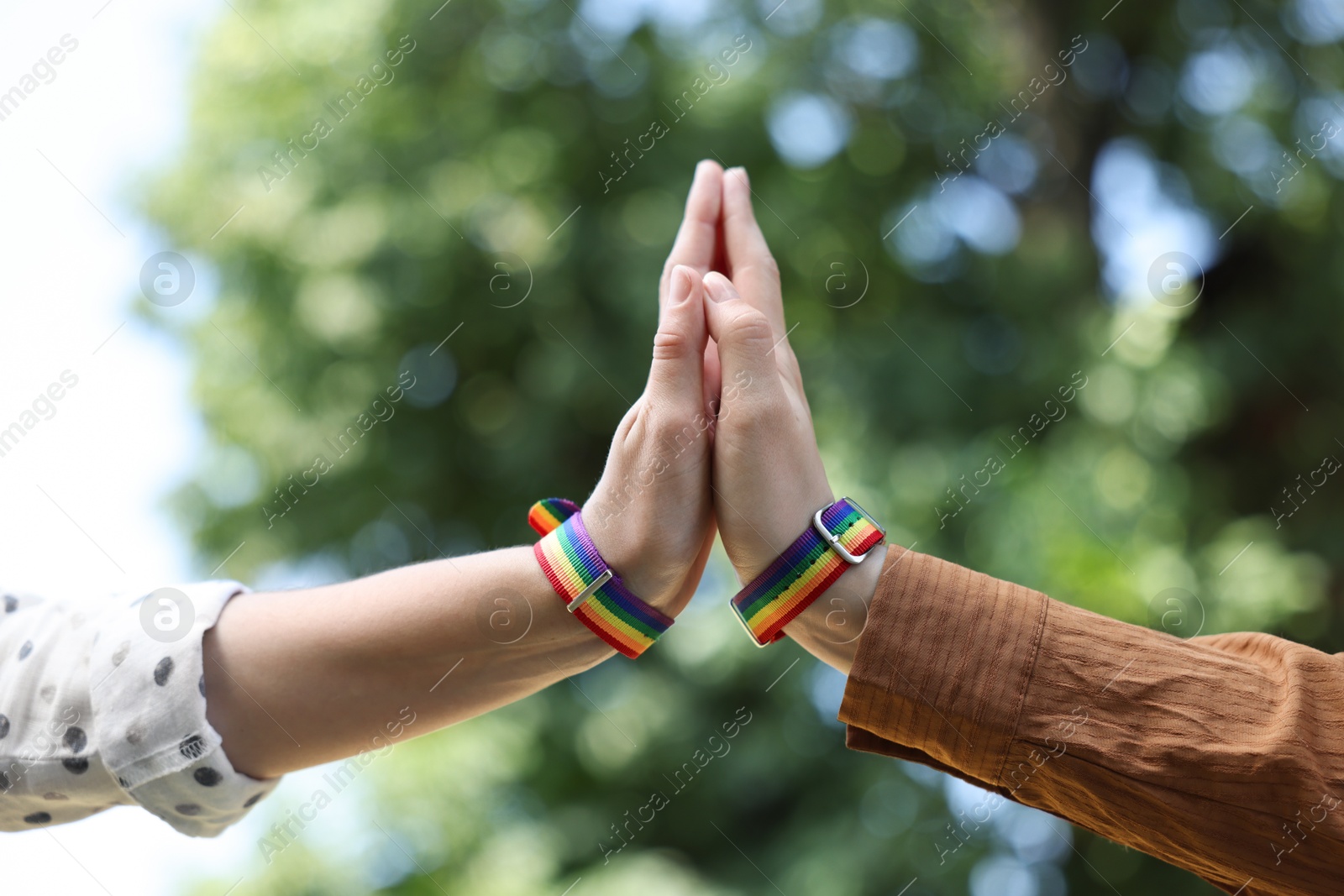 Photo of LGBT concept. Women in rainbow wristbands holding hands outdoors, closeup