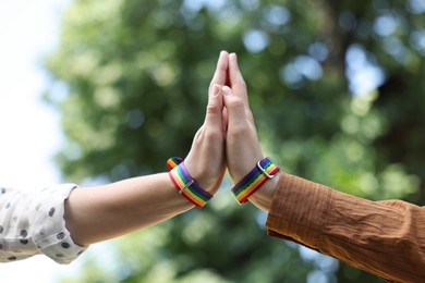 Photo of LGBT concept. Women in rainbow wristbands holding hands outdoors, closeup
