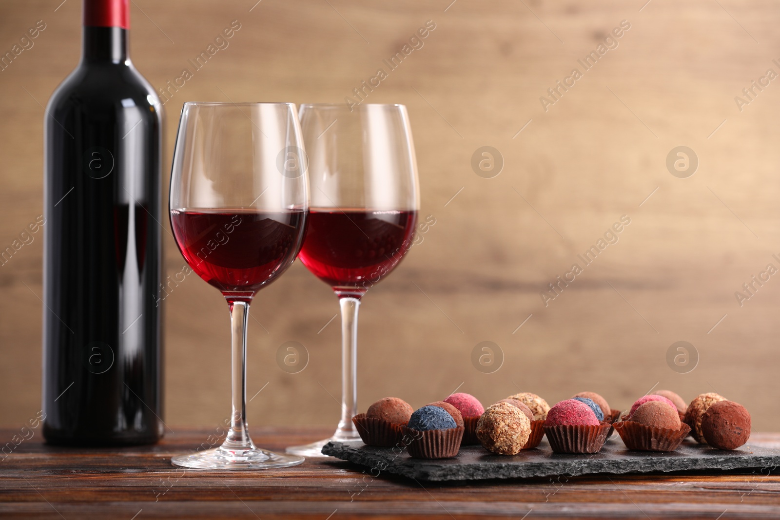 Delicious truffle bonbons and wine on wooden table. Space for text Photo of Delicious truffle bonbons and wine on wooden table. Space for text