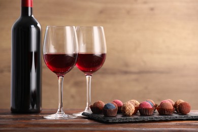 Photo of Delicious truffle bonbons and wine on wooden table. Space for text