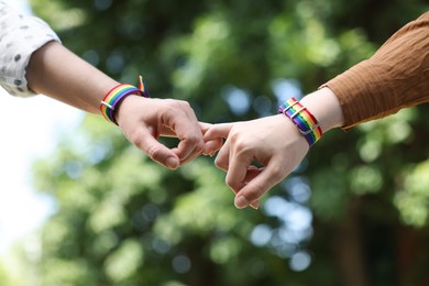 Photo of LGBT concept. Women in rainbow wristbands holding hands outdoors, closeup