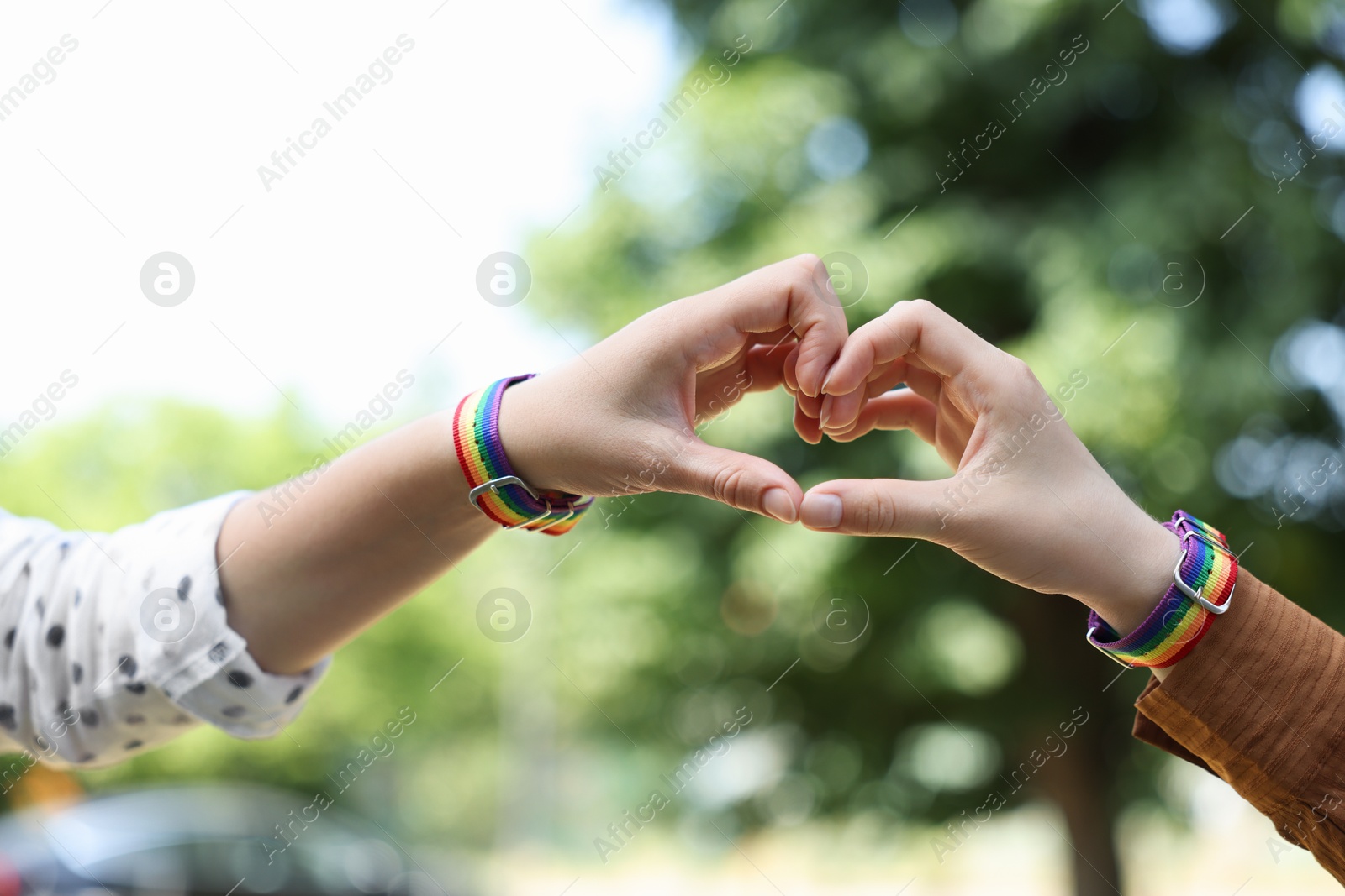 LGBT concept. Women in rainbow wristbands making heart shape outdoors, closeup Photo of LGBT concept. Women in rainbow wristbands making heart shape outdoors, closeup