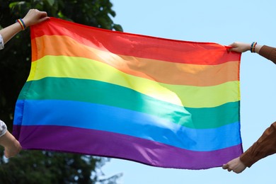 Photo of LGBT concept. Women in rainbow wristbands with flag outdoors, closeup