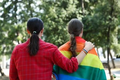 Photo of LGBT concept. Women in rainbow wristband with flag outdoors, back view