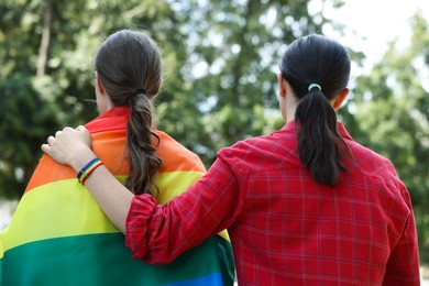 Photo of LGBT concept. Women in rainbow wristband with flag outdoors, back view