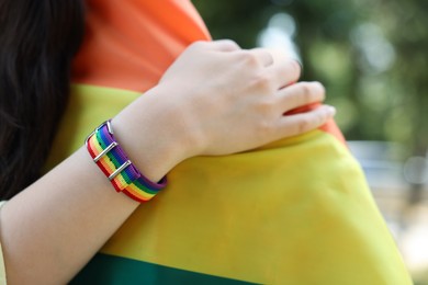 Photo of LGBT concept. Women in rainbow wristband with flag outdoors, closeup