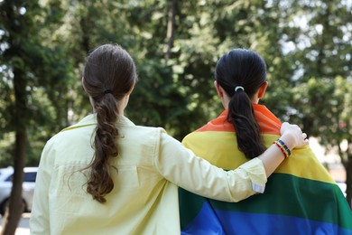 Photo of LGBT concept. Women in rainbow wristband with flag outdoors, back view