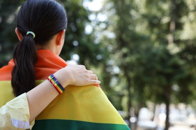 Photo of LGBT concept. Women in rainbow wristband with flag outdoors, back view. Space for text