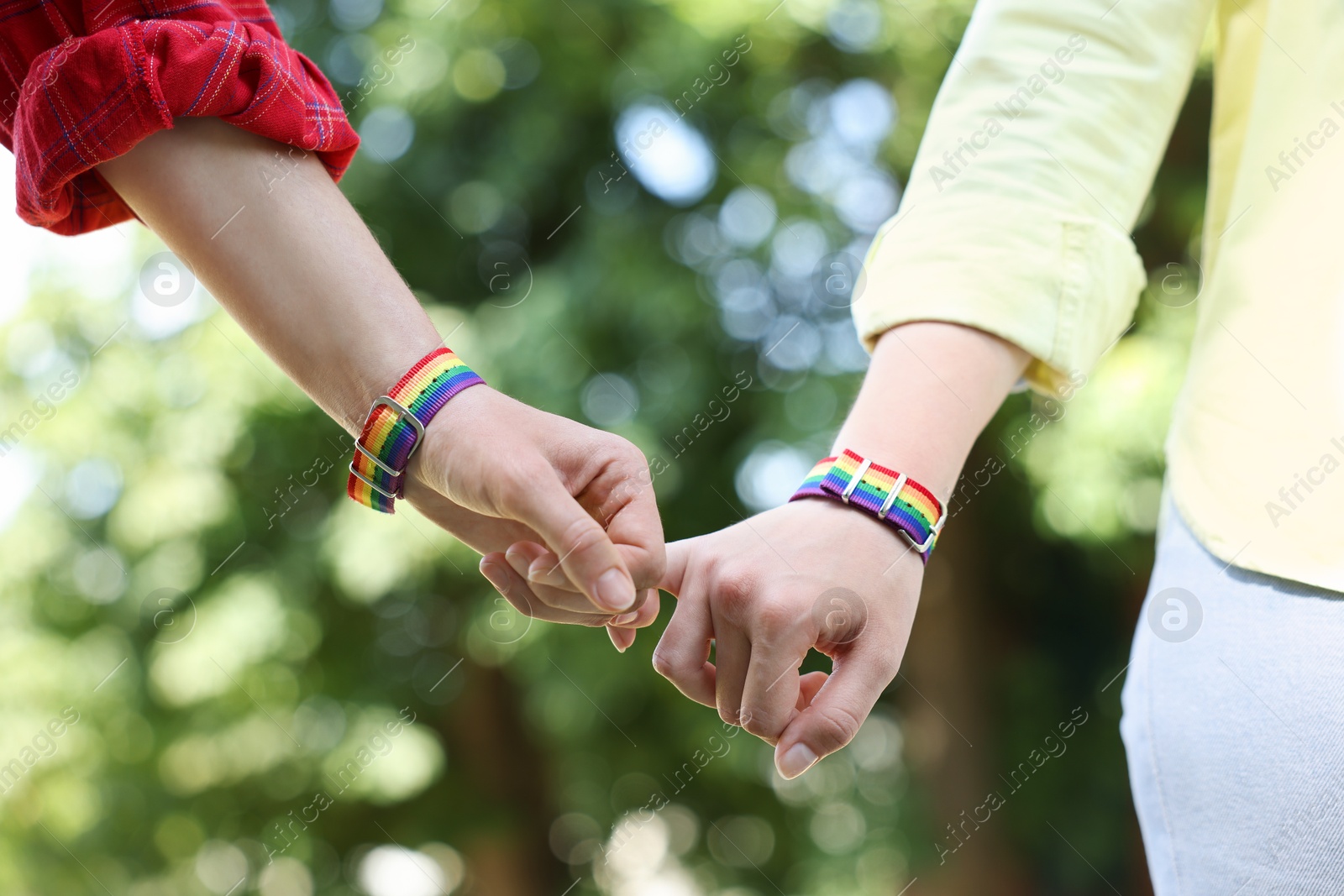 Photo of LGBT concept. Women in rainbow wristbands holding hands outdoors, closeup