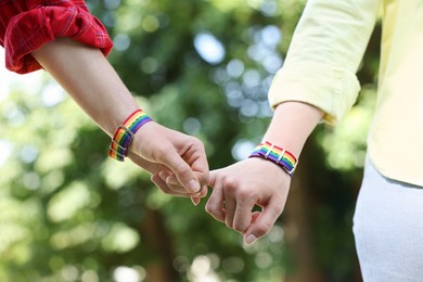 Photo of LGBT concept. Women in rainbow wristbands holding hands outdoors, closeup
