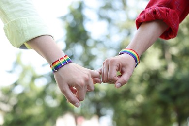 Photo of LGBT concept. Women in rainbow wristbands holding hands outdoors, closeup