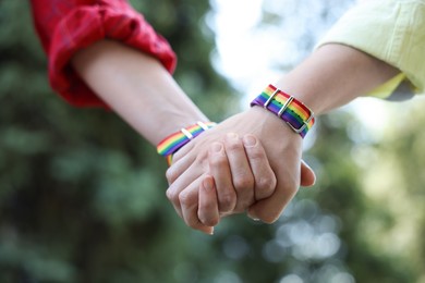 Photo of LGBT concept. Women in rainbow wristbands holding hands outdoors, closeup