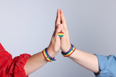 Photo of LGBT concept. Women in rainbow wristbands with heart shaped pin holding hands on light grey background, closeup