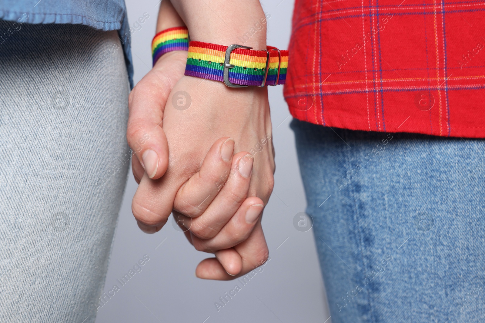 Photo of LGBT concept. Women in rainbow wristbands holding hands on light grey background, closeup