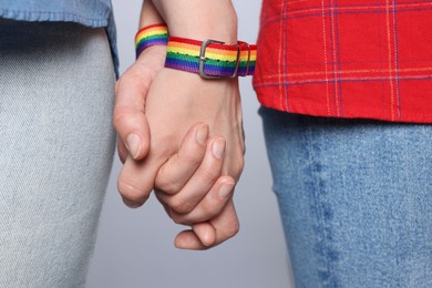 Photo of LGBT concept. Women in rainbow wristbands holding hands on light grey background, closeup