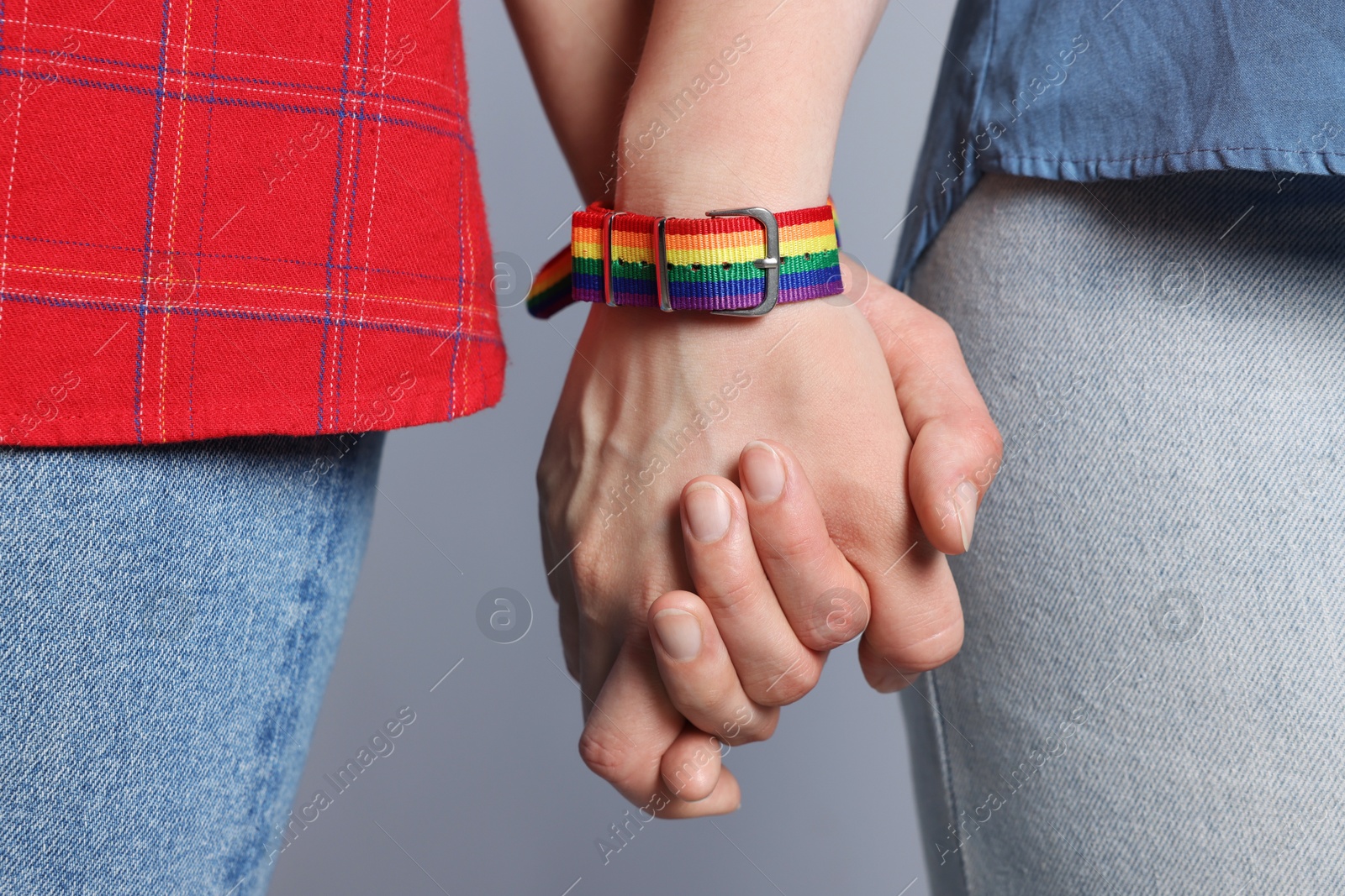 Photo of LGBT concept. Women in rainbow wristbands holding hands on light grey background, closeup
